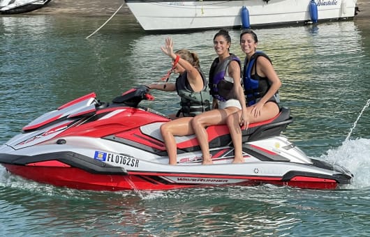 Três meninas, todas usando coletes salva-vidas, sorrindo enquanto andavam com segurança em um jet-ski.